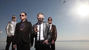 four men in suit jackets and black pants standing near mountain cliff during daytime HD wallpaper