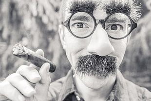 close up grayscale shot of man holding tobacco and wearing eyeglasses