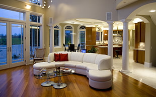 white sectional couch on brown wooden floor near three white columns in living room