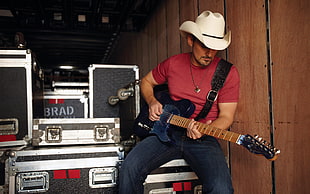 white cowboy hat, red t-shirt, and blue denim jeans, and black electric guitar