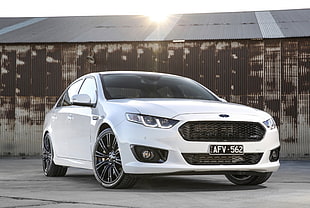 white Ford sedan with gray barn background