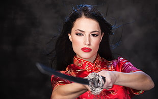 woman wearing red and brown floral qipao holding silver dragon sword