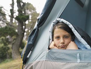 girl covered with black and white sleeping bag inside gray and black tent during day time