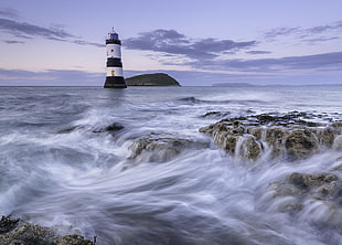 photo of white and black lighthouse in middle of body of water, penmon, anglesey