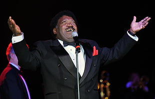 man in black dress suit raising his hands with microphone