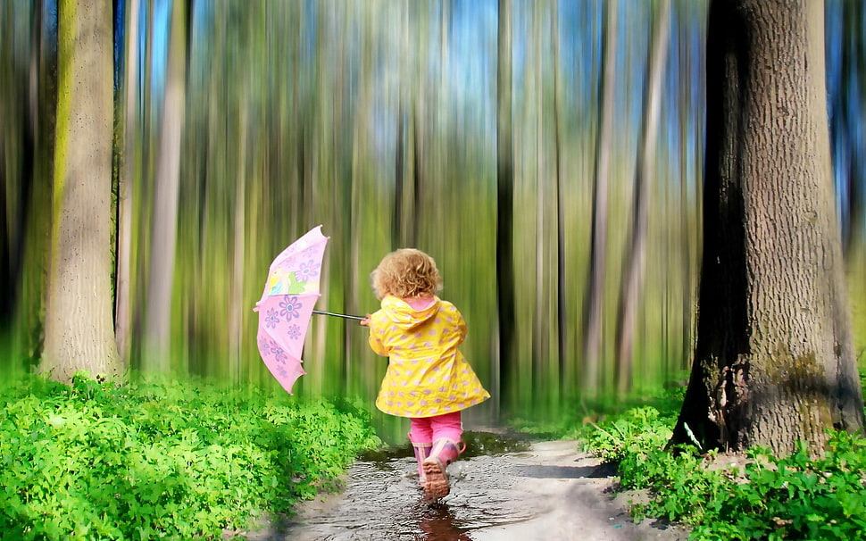 toddler girl in yellow hoodie holding purple floral umbrella beside brown bark trees HD wallpaper