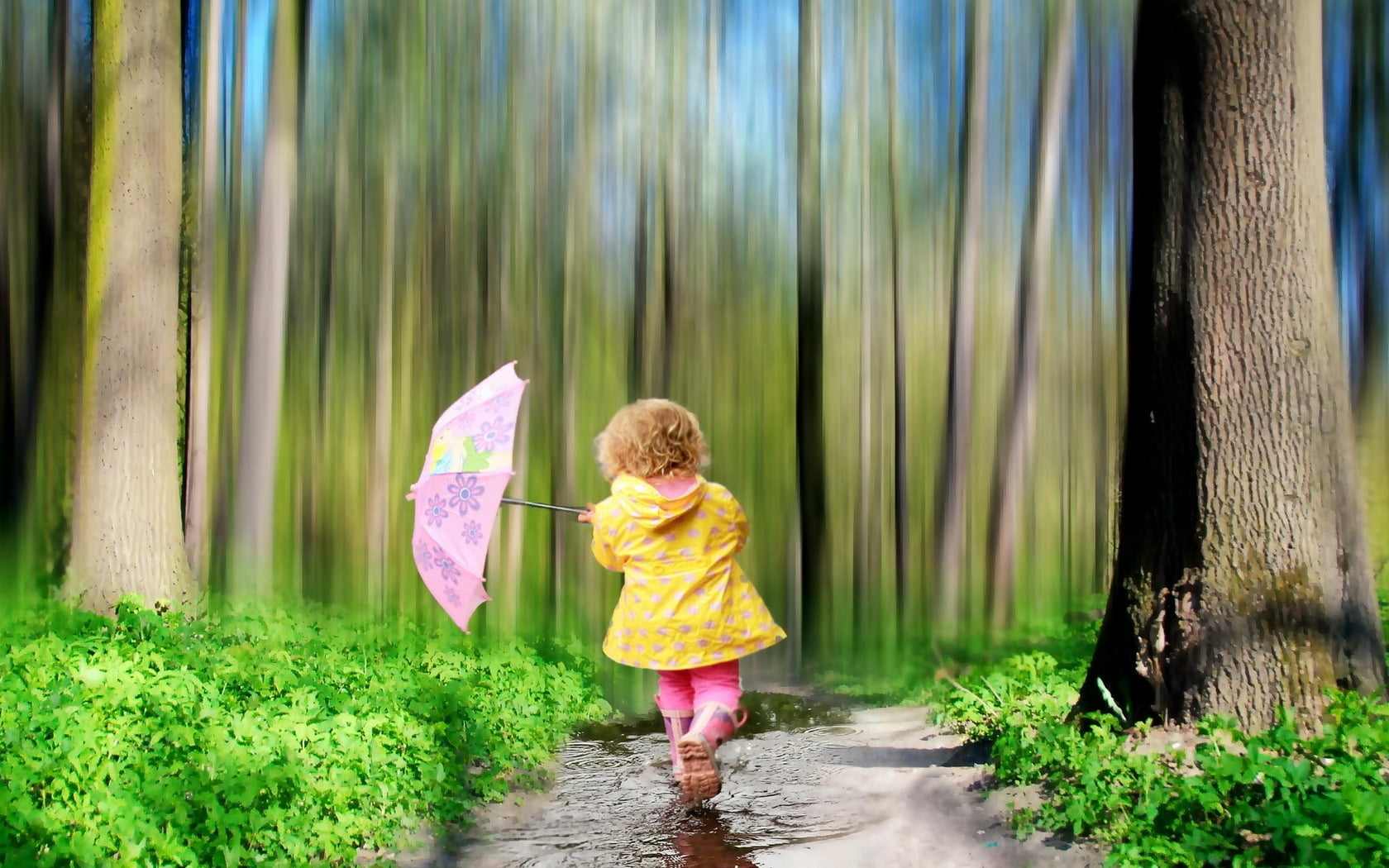 toddler girl in yellow hoodie holding purple floral umbrella beside brown bark trees