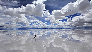 person walking on sea under blue and white sky