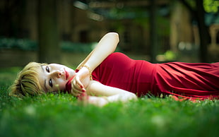 depth of field of woman in red dress lying on green grass
