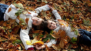 two girls lying on the ground covered with wilted leaves
