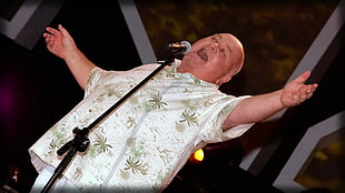 man in white and green plant print polo t-shirt stands near microphone