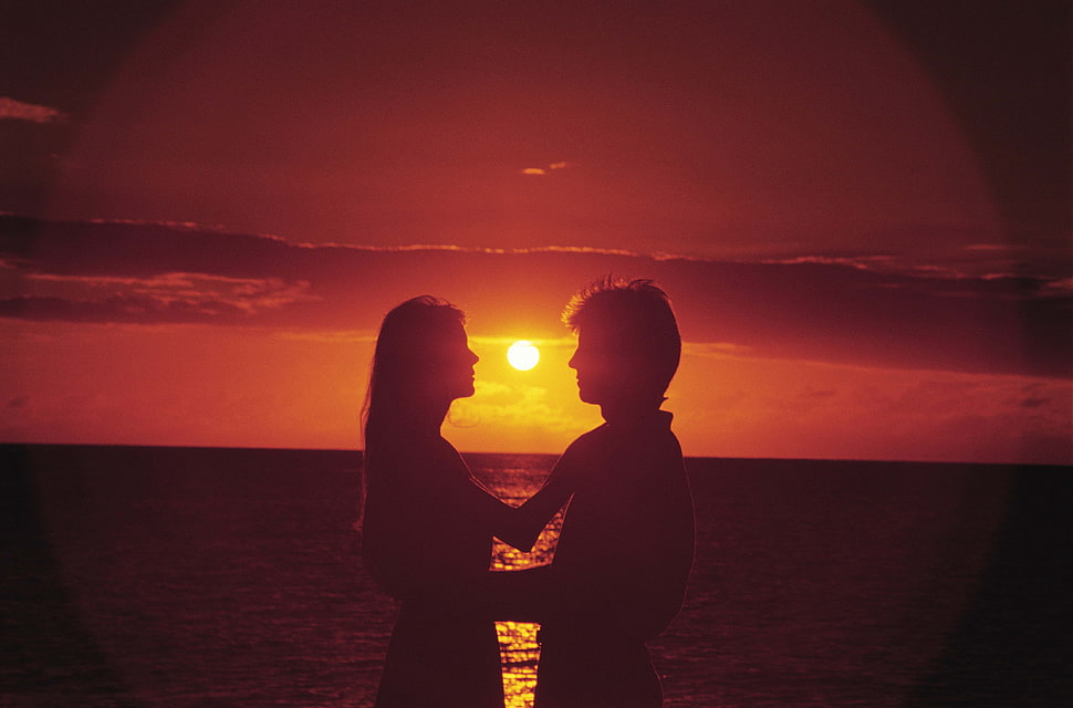 silhouette photo of man and woman near ocean during golden hour HD wallpaper