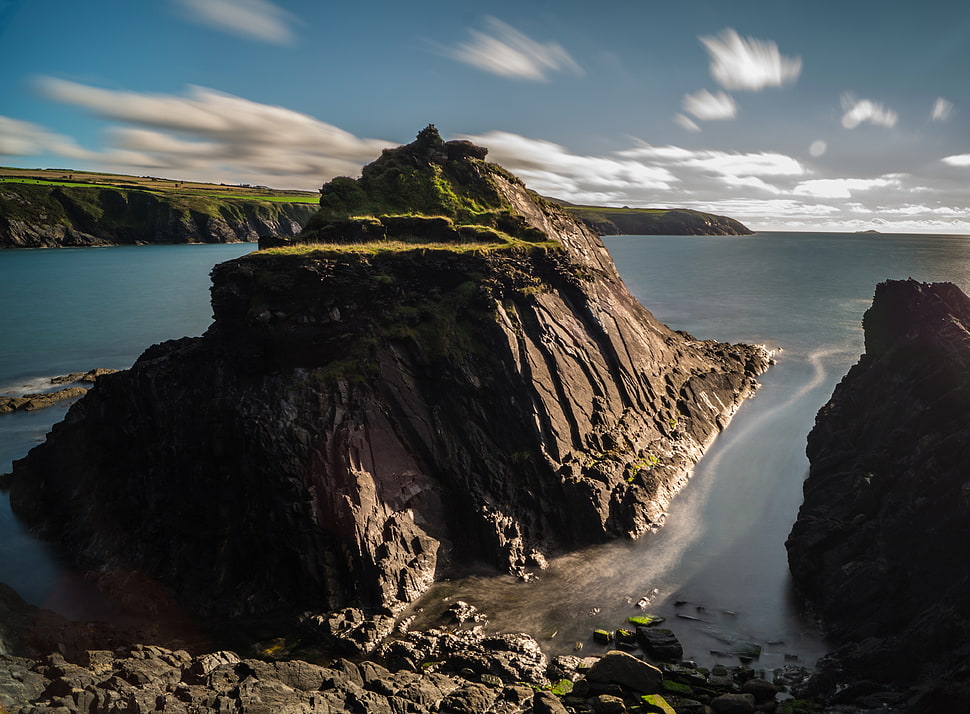 brown and green rock mountain in front of body of watyer HD wallpaper