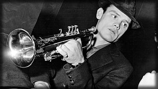 gray scale man wearing coat and hat playing trumpet
