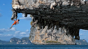 man climbing rock formation during daytime HD wallpaper