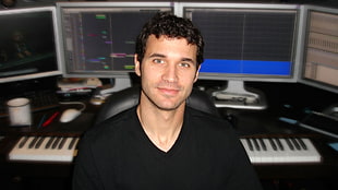 man in black v-neck t-shirt behind four grey flat screen monitors