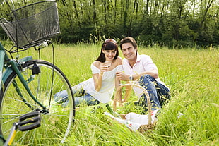 panoramic photo of couple sitting on green grass field near green bicycle HD wallpaper