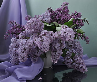 shallow focus photo of white and purple Lilac flowers in white ceramic vase centerpiece