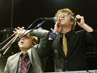 man singing on mic beside man holding pair of drum sticks