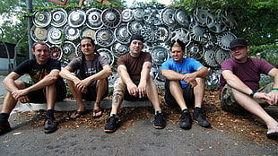 five men sitting on concrete path in front of wheel hub caps
