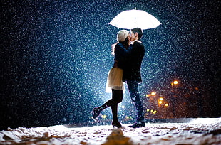 man and woman holding umbrella kissing under rain