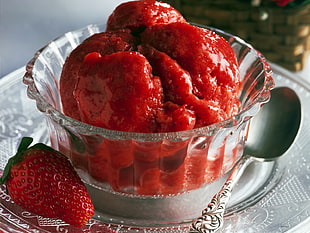 mashed strawberry on clear cut glass bowl beside stainless steel spoon