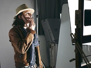 man wearing brown long-sleeved top and cowboy hat while smoking