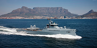 white P001 naval ship carrying two boats cruising open water overlooking mountains during daytime