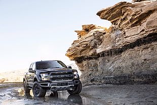 gray Ford Ranger pickup truck beside cliffs with boulders