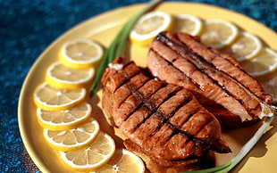 shallow focus photography of fried fish surrounded of green chives and sliced lemon served on yellow plate