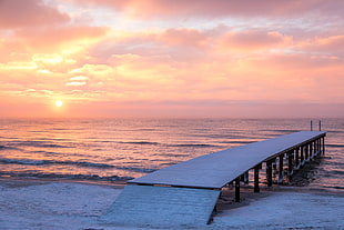 white wooden dock beside the beach during sunset