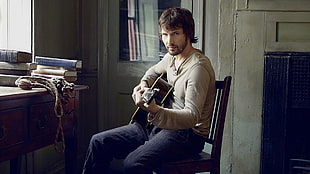 man in gray long-sleeve shirt seating using guitar