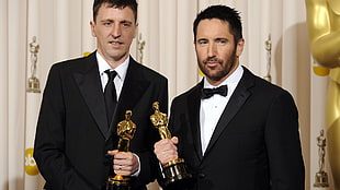 two men in black formal suit jackets holding trophies