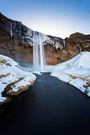 snow coated cascading brown rock waterfall and river photo, iceland