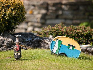 shallow depth photography of miniature scarecrow  and rv trailer on grass field