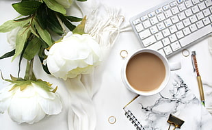 mug of coffee beside pen, spiral notebook and keyboard