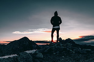 man in black hoodie standing on stone at daytime