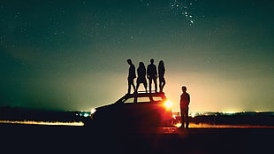 silhouette photography of people standing on top of car during night time