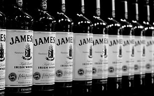 selective focus gray scale photo of lined James Whisky bootles