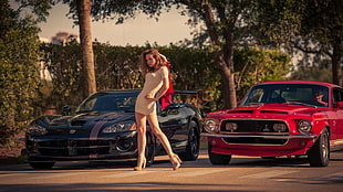 woman wearing white scoop-neck puff-sleeved mini dress standing beside black Dodge Viper and classic red Ford Mustang Shelby during daytime