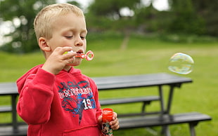 boy wearing red jacket playing bubbles