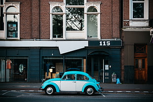 white and teal classic Volkswagen Beetle on side of road near brown and black concrete building during daytime