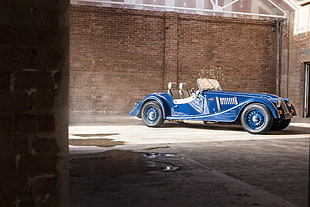 classic blue convertible car beside brown brick wall