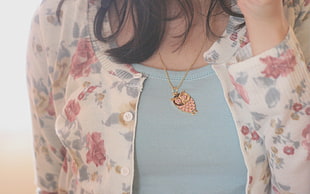 closeup photo of woman wearing white and gray floral top and gold-colored owl pendant