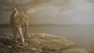 two men standing on boulder rock beside sea photography