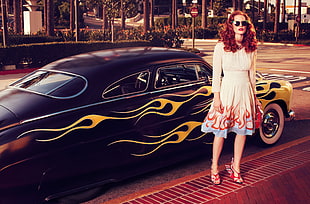red haired woman in white long-sleeved dress standing beside blue and yellow sports car