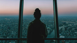 silhouette of woman facing glass wall overlooking city