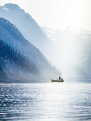 person fishing on boat on the sea near on mountains during daytime