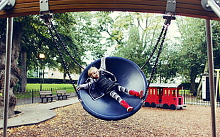 boy in blue jacket swinging on round dome swing