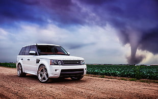 white Range Rover parked on soil road with view of tornado